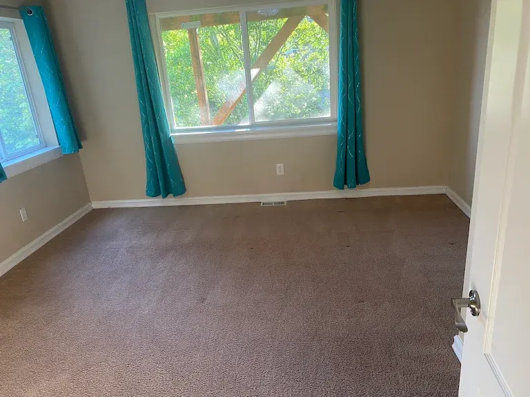 Clean brown carpet in an empty bedroom with teal curtains