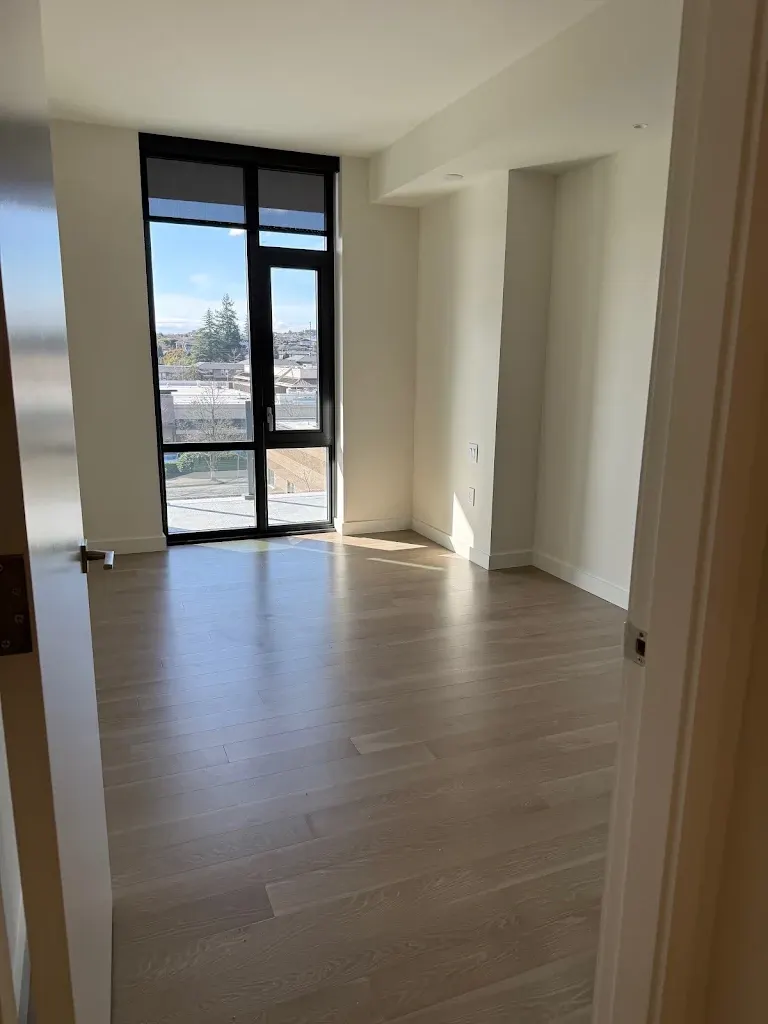 Empty condo room with light hardwood and a floor-to-ceiling window