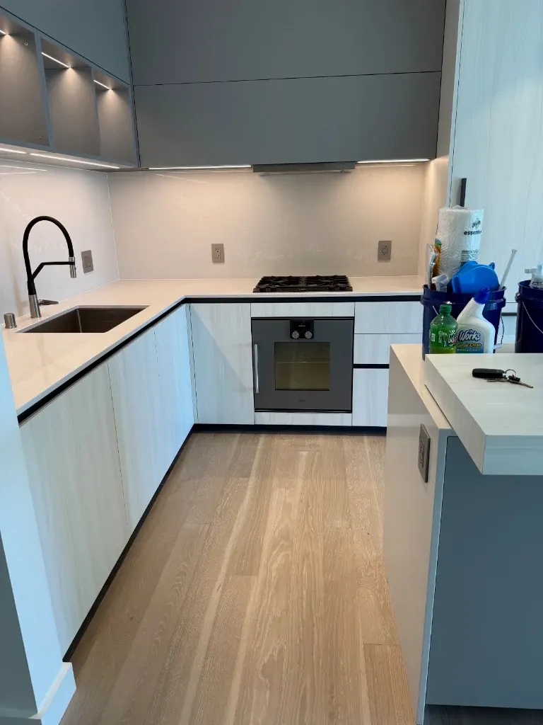 Modern condo kitchen with white cabinets and light hardwood floor after a move-out clean
