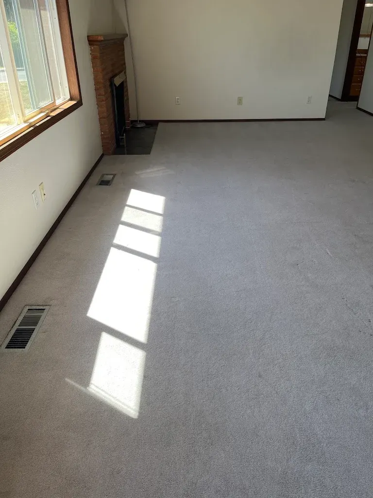Light gray carpet cleaned in an empty living room with a brick fireplace